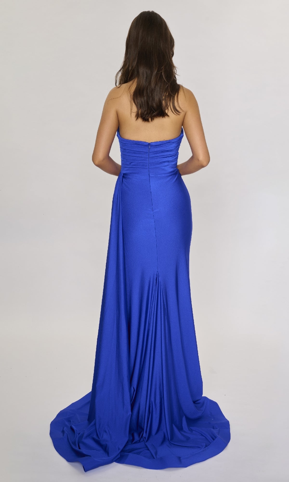 A woman faces away, wearing the Nina Canacci 6686 long formal dress—a royal blue, strapless evening gown with a sweetheart neckline and slight train—set against a plain light background.